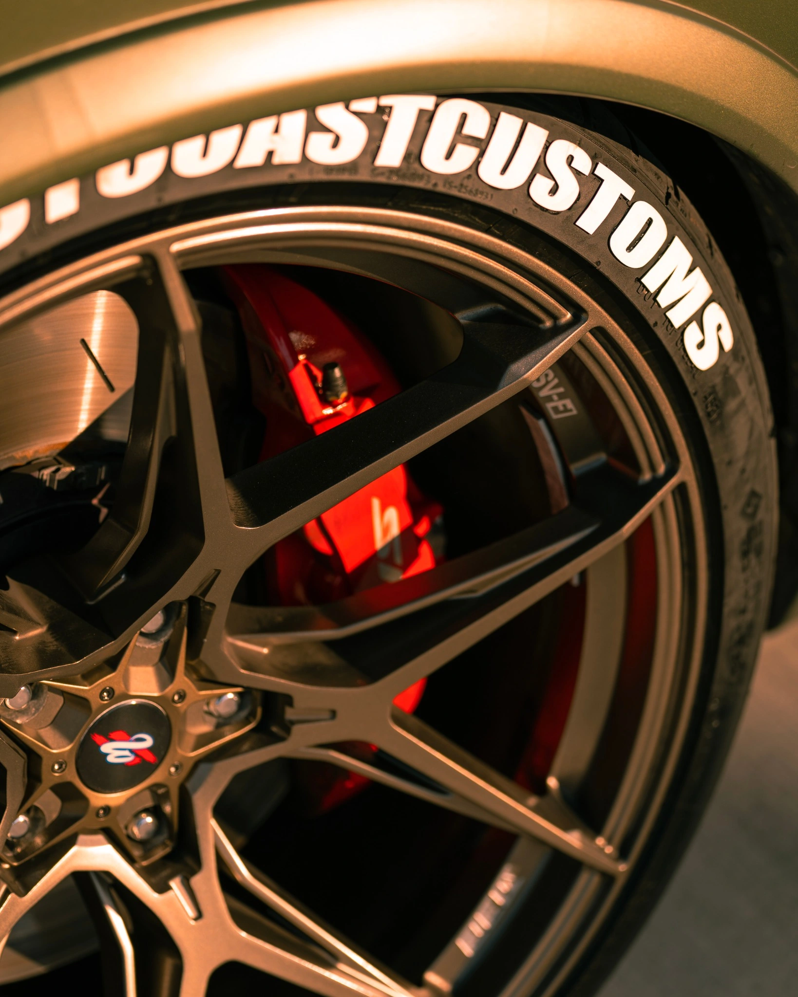 Close-up of a custom wheel, red brake caliper and tire lettering in warm sunlight